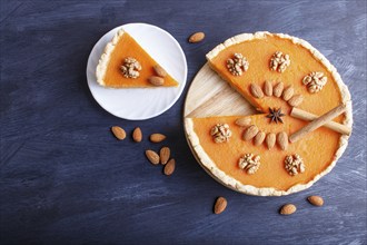 Traditional american sweet pumpkin pie decorated with nuts, on dark blue wooden background. top