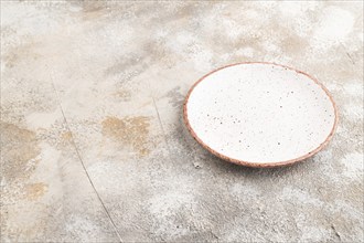 Empty white with dots ceramic plate on brown concrete background. Side view, copy space