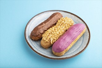 Set of eclair, traditional french dessert on ceramic plate on blue pastel background. side view,