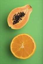 Ripe cut papaya and orange on green pastel background. Top view, flat lay, close up. Tropical,