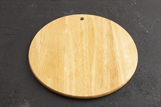 Empty round wooden cutting board on black concrete background. Side view, close up