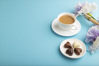 Cup of cioffee with chocolate candies and lilac iris flowers on blue pastel background. side view,