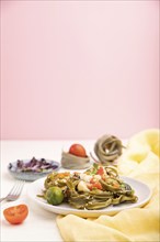 Tagliatelle green spinach pasta with tomato, pea and microgreen sprouts on a white and pink