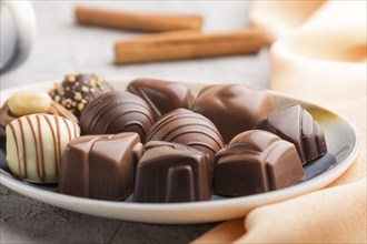 Different chocolate candies and a cup of coffee on a gray concrete background and orange textile.