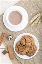 Homemade oatmeal cookies with a cup of cocoa on a linen textile and white wooden background. top