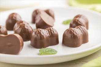 Chocolate candies with almonds on a white wooden background and green textile. side view, close up,