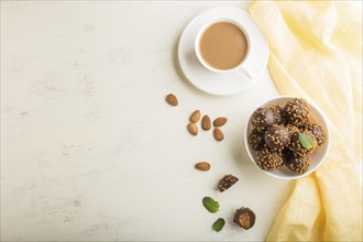 Chocolate caramel ball candies with almonds and a cup of coffee on a white wooden background and