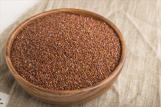 Wooden bowl with raw red quinoa seeds on a white wooden background and linen textile. Side view,