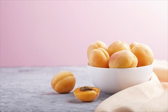 Fresh orange apricots in white bowl on gray and pink pastel background. side view, copy space,