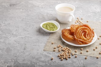 Traditional indian candy jalebi in white plate with mint chutney on a gray concrete background.