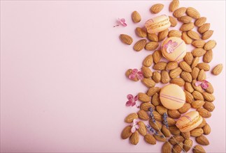 Orange macarons or macaroons cakes with almond nuts on pastel pink background. top view, flat lay,