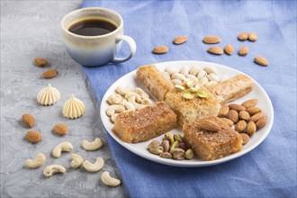 Traditional arabic sweets (basbus, kunafa, baklava), a cup of coffee and nuts on a gray concrete