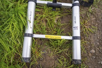 A metal ladder lies on a grass- and dirt-covered ground surface, fibreglass installation, Calw