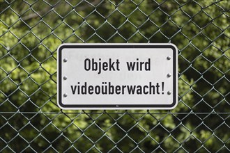 Sign mounted on a green wire mesh fence with the inscription: Objekt wird videoüberwacht! in