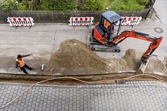 Construction workers lay fibre optic cable in trench under asphalt, cable trench, excavator,