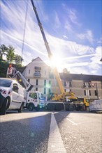 A lifting crane and construction workers during construction work on a sunny street in front of