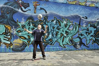 A ten-year-old boy plays with his football in front of a graffiti wall, Germany, Europe