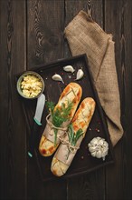 Baguette with garlic butter and herbs, fried, on a brown wooden table, top view, rustic style, no