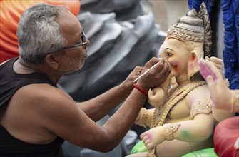 An artisan gives final touches to an idol of the elephant-headed Hindu deity Ganesha at a workshop