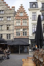 Narrow historic façade in a lively street with street cafés and pedestrians, Ghent