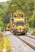 Yellow tractor moving on a railway track through a densely wooded area, Hermann Hesse Bahn track