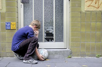 Crying ten-year-old boy Ten-year-old in front of the smashed glass pane on a front door, Germany,