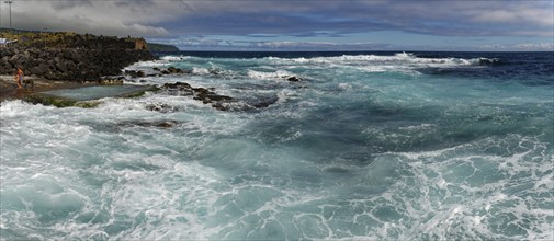 Stormy waves crash against a rocky shore under a cloudy sky, seawater bathing establishment,