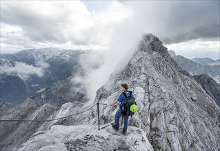 Mountaineer on a narrow rocky ridge on a steel cable, Watzmann crossing to Watzmann Mittelspitze,