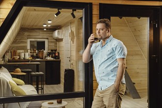 A man enjoys juice while standing on terrace of log cabin late at night