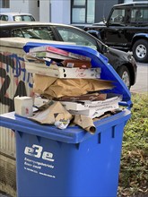 Overflowing waste paper bin, standing on a pavement, waiting to be emptied by a municipal waste