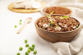 Quinoa porridge with green pea and chicken in wooden bowl on a white wooden background and linen