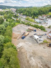 Large-scale aerial view of a construction site with machines, surrounded by trees and buildings,