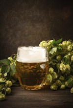 A mug of beer, on a wooden table, with a branch of fresh hops, rustic, no people