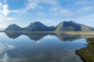 Aerial view over the calm sea to Mt. Brunnhorn and Vestrahorn, east of Höfn, clouds are reflected