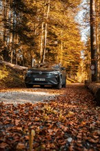 Car on autumnal forest road with orange leaves, electric car VW ID5, Gechingen, Black Forest,