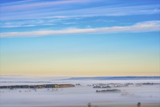 Morning fog over a rural plain landscape with hills and trees above the fog and a view to the