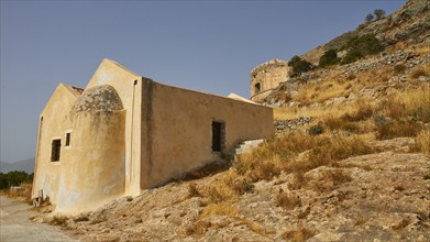 A historic building on a hillside with dry vegetation and mountains in the background, Venetian Sea