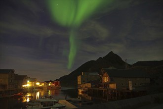 Glowing green aurora borealis over a fjord with houses and mountains at night, winter, Nyksund,