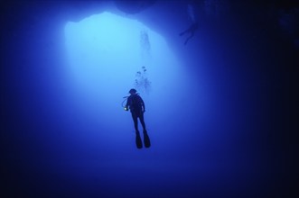 Female diver scuba diver diving in floating under opening cave opening large hole in seabed