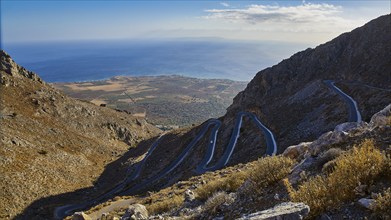 Serpentine road winds through a dry mountainous landscape down to the sea, Kallikratis, Kallikratis