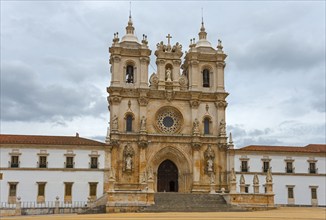 Majestic Gothic monastery façade with ornate towers against a cloudy sky, Mosteiro de Alcobaça,