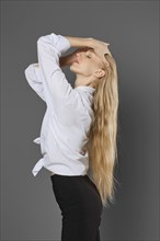 A young woman stands in profile lifting hair and showing her long hair