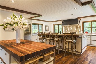 Country style kitchen with island and rustic wooden high chairs inside a New Hampton style home,