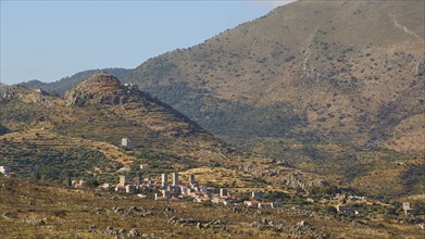 View of a quiet rural village surrounded by mountainous landscape under a clear blue sky,