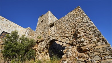 Weathered stone wall of a fortress with arches and surrounding vegetation, Vathia, residential