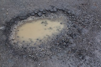 Pothole filled with rainwater on wet black asphalt road surface in spring, Montreal, Quebec,