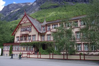 Historic Victorian-style building surrounded by green mountains and trees with striking red