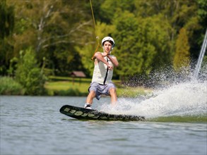 Young man on wakeboard in splashing water, cheerful, water skiing and wakepark, water sports