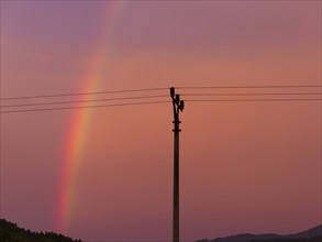 Red sky with rainbow, electricity pylon and power lines