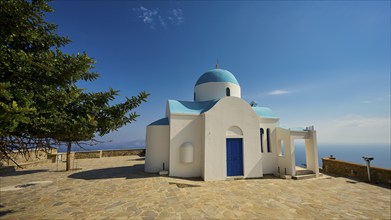 White-blue church with a tree next to it under a blue sky, Church of Profitis Ilias, above Nikia,